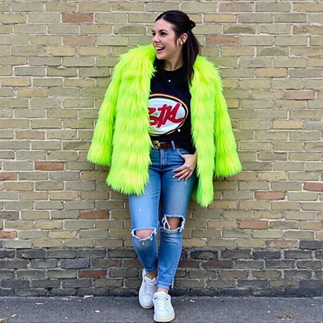 Photograph of a bold outfit featuring a neon green faux fur coat, a graphic t-shirt, ripped jeans, and chunky sneakers, leaning against a brick wall.